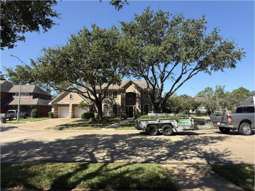 Residential property with a truck and trailer parked on the driveway under large oak trees.