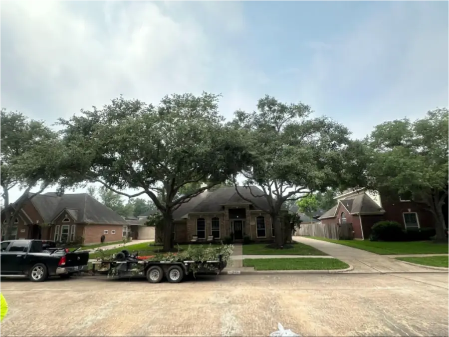 A house with large trees in the front yard and a trailer parked on the street.